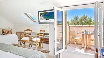 Ein Schlafzimmer mit einem Bett, einem Schreibtisch und einem Sessel, sowie ein Balkon mit Tisch und Stühlen und einem Fernseher, der einen Strand zeigt.