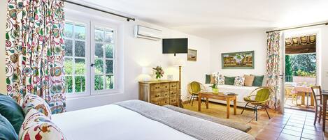 Ein Schlafzimmer mit einem großen Bett, einer Holzkommode, einem Schreibtisch mit Stuhl, einem an der Wand montierten Fernseher und einem Fenster mit Vorhängen.