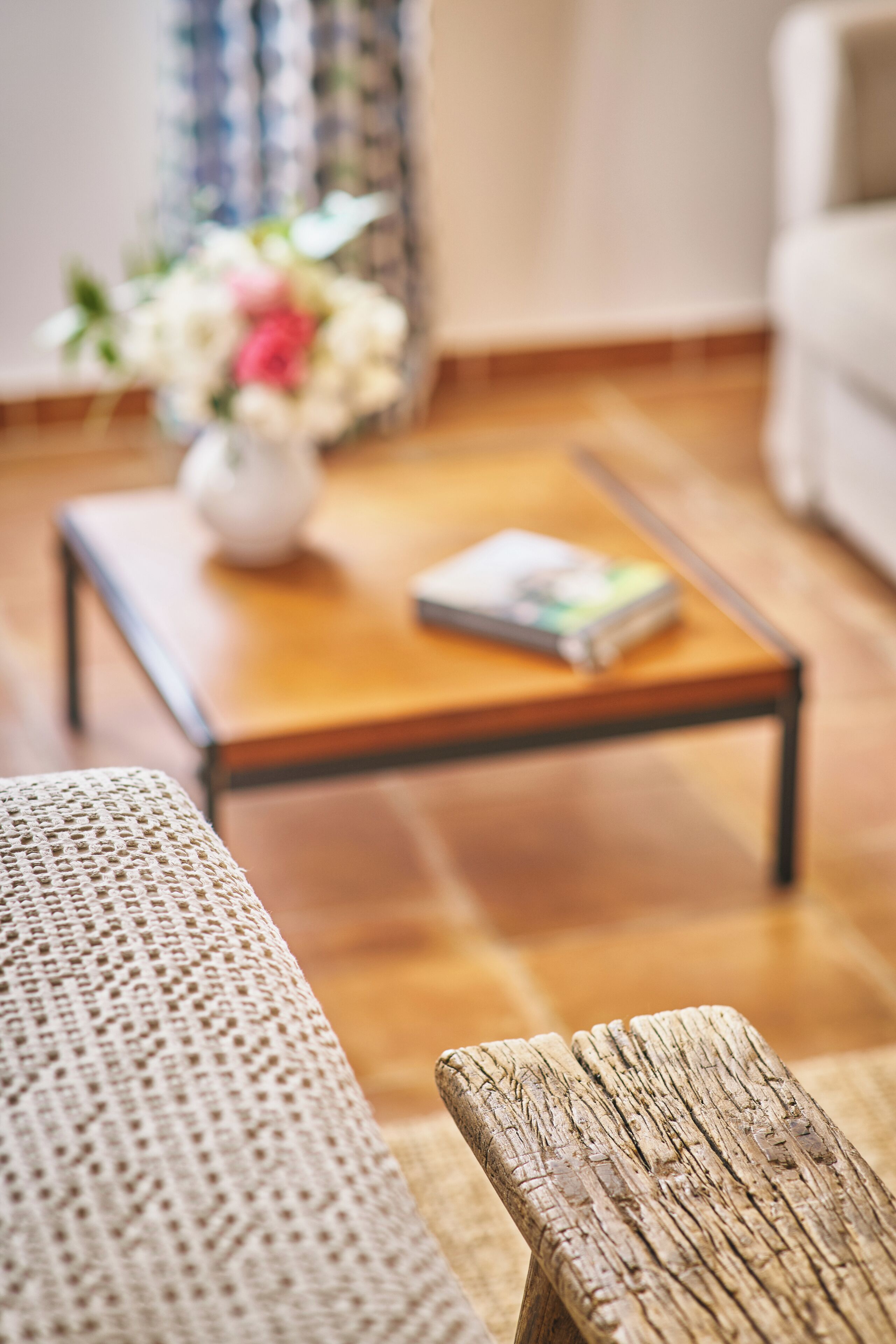 Un salon avec une table basse en bois, un canapé blanc et un vase décoratif rempli de fleurs.