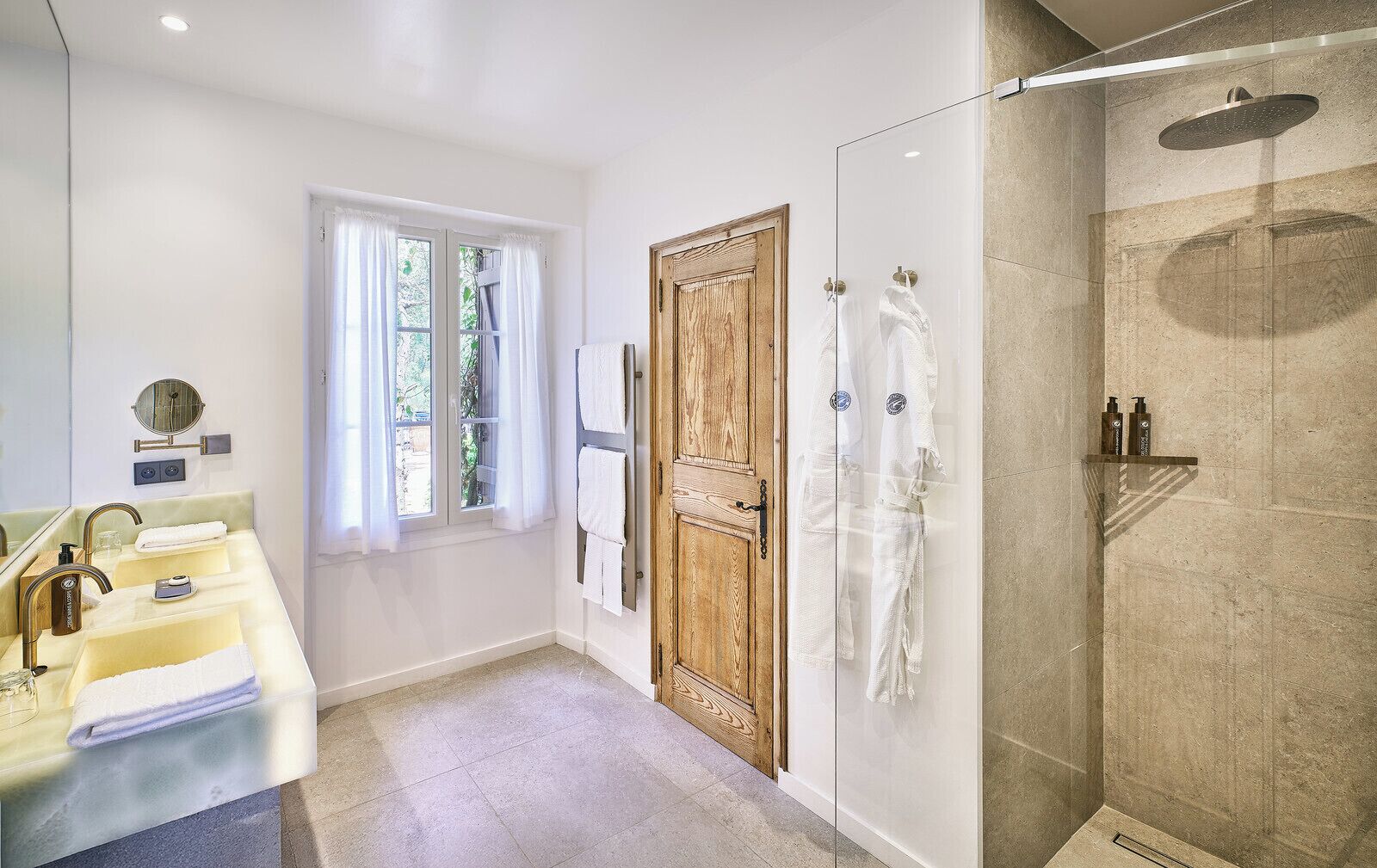 Une salle de bain moderne avec un grand miroir, deux lavabos, une porte en bois et une douche séparée par des parois de verre.