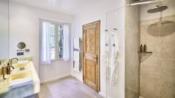 Une salle de bain moderne avec un grand miroir, deux lavabos, une porte en bois et une douche séparée par des parois de verre.