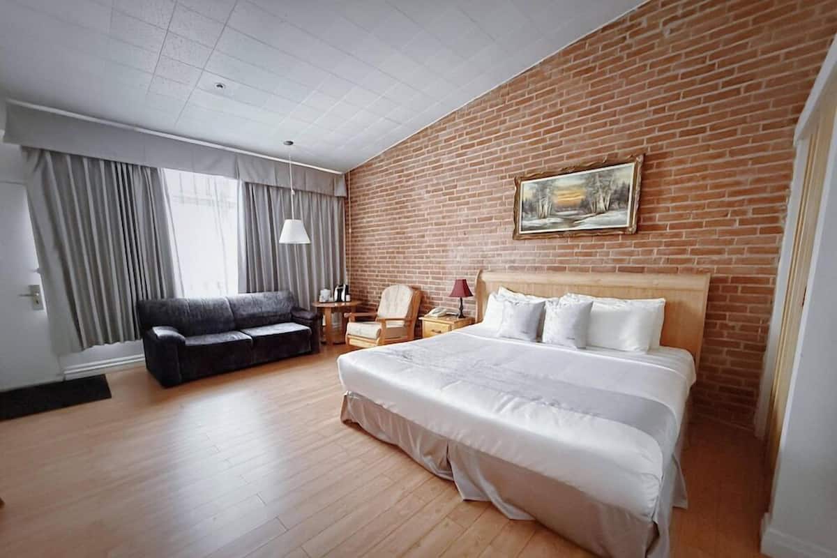 Ein Hotelzimmer mit einem großen Bett, einer Couch, einem Schreibtisch mit Lampe und einem Gemälde an der Backsteinwand.