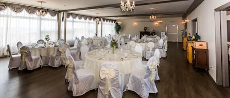 A banquet hall with round tables, white tablecloths, and chairs with white covers.
