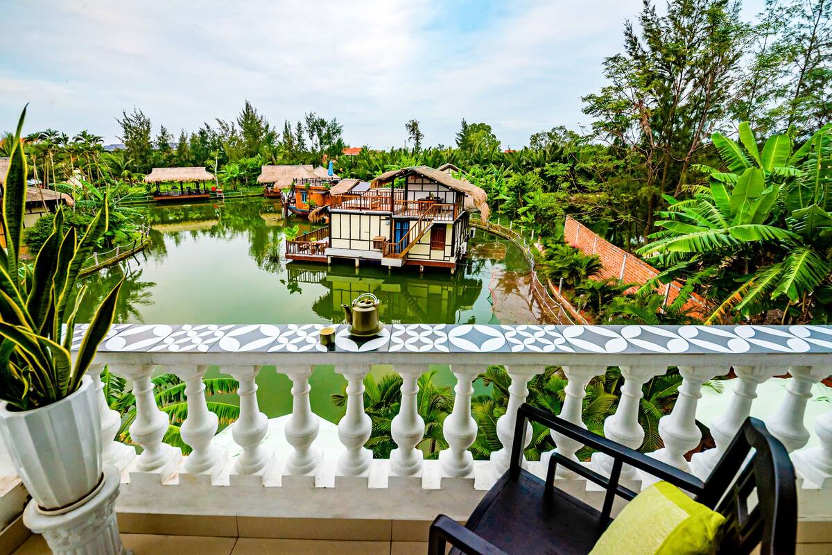 A floating house with a thatched roof, surrounded by lush greenery and a calm water body.