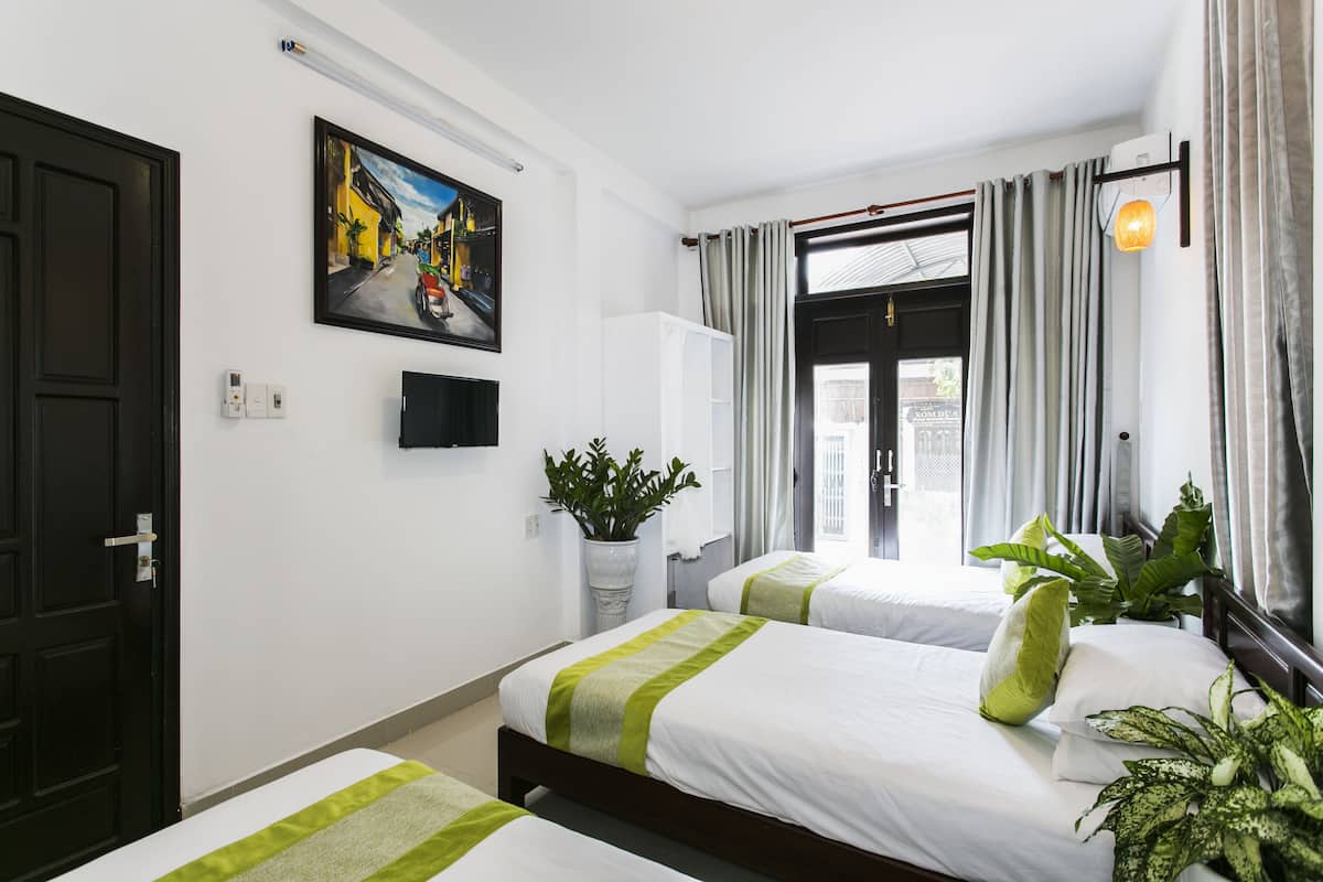 A hotel room with two beds, a potted plant, a painting, and a window with curtains.