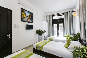 A hotel room with two beds, a potted plant, a painting, and a window with curtains. - Coconut Hamlet Homestay (Da Nang)