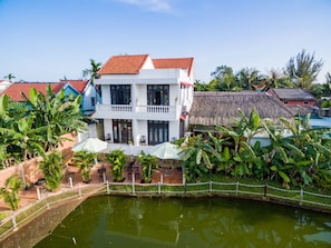 A two-story building with a red-tiled roof, a balcony, and a pool area surrounded by lush greenery.
