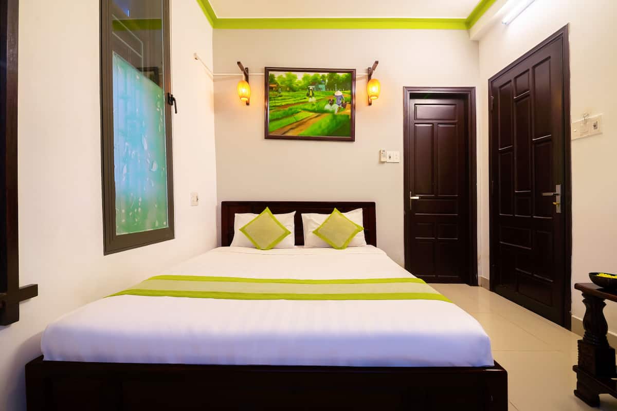 A hotel room with a bed, a painting, and two doors.