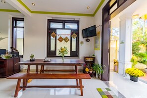 A dining area with a wooden table and bench, a vase with flowers, and a window with decorations. - Coconut Hamlet Homestay (Da Nang)