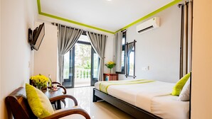 Une chambre d’hôtel avec un lit, une chaise, une petite table sur laquelle est posé un vase de fleurs, et une fenêtre avec des rideaux.