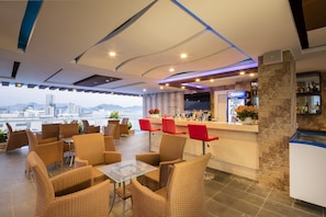 Un bar moderno con mobiliario de mimbre, una barra con refrigerador de Pepsi y vistas a un paisaje urbano.