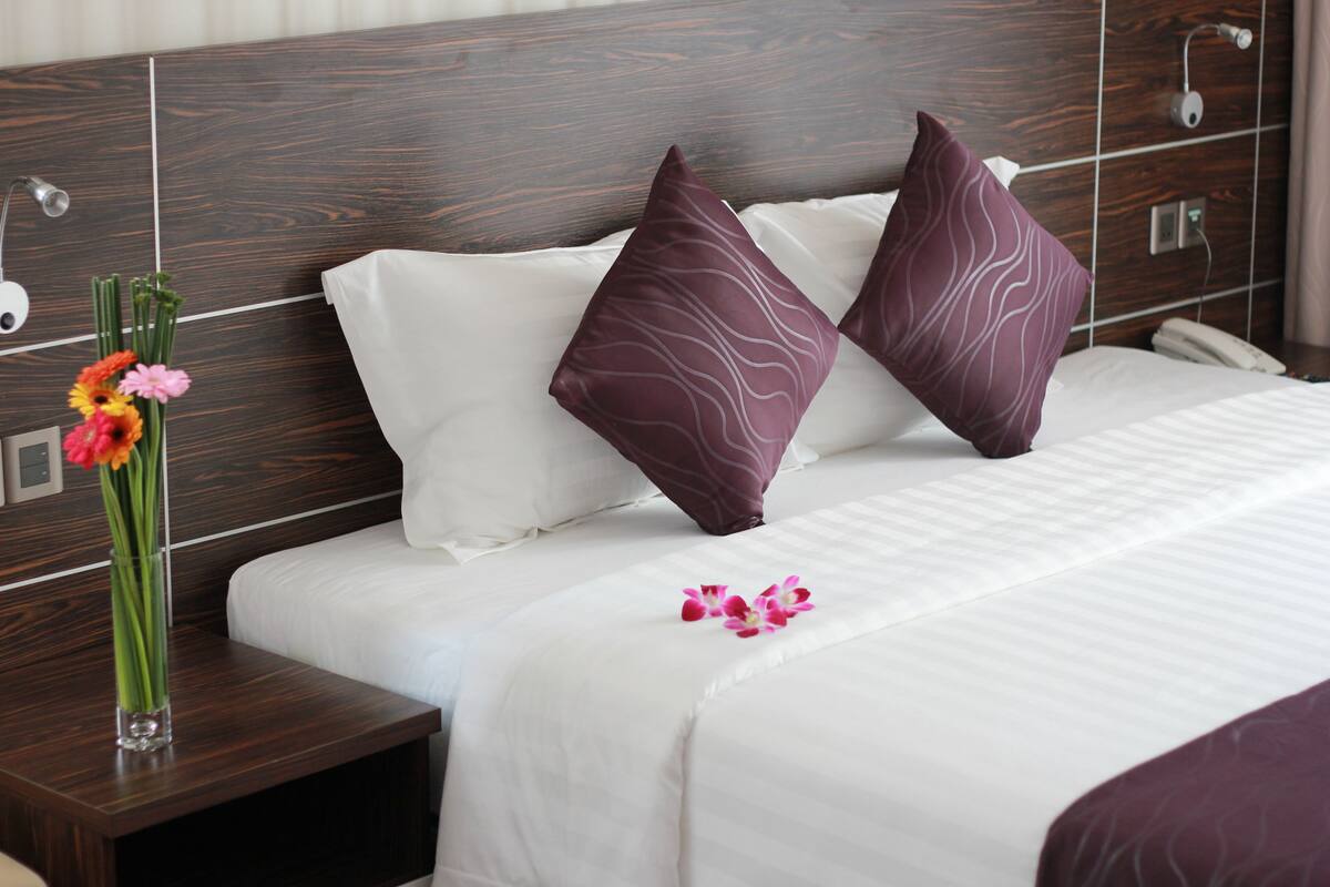 Une chambre d’hôtel avec une tête de lit en bois, du linge de lit blanc et un vase rempli de fleurs sur la table de chevet.