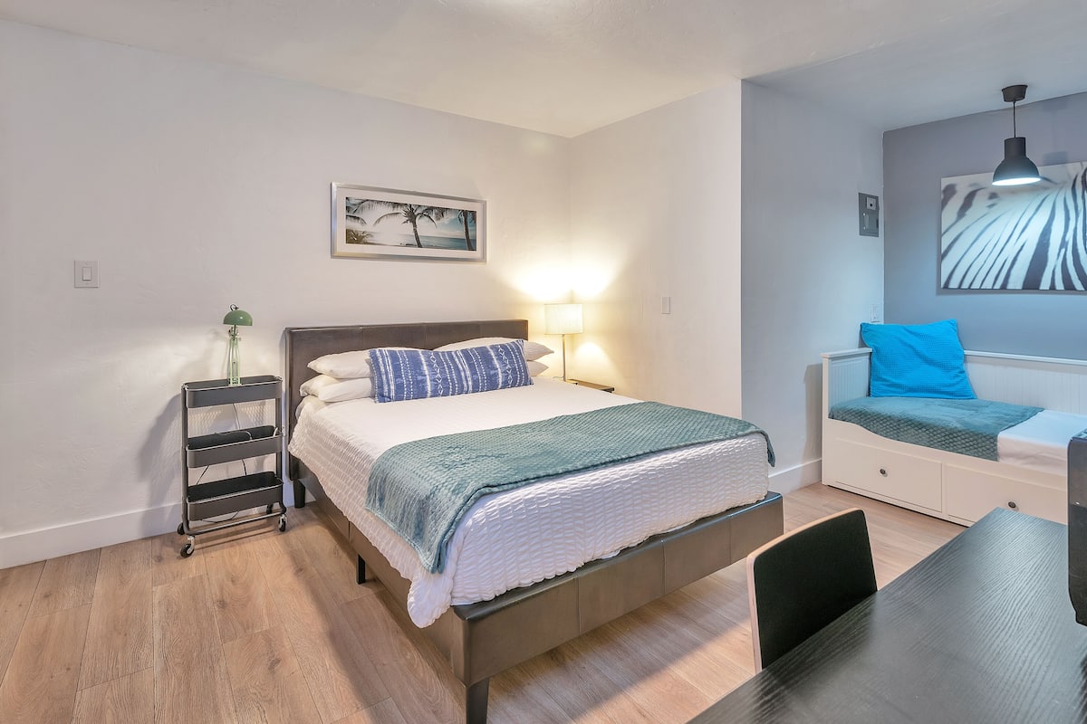 A bedroom with a bed, bedside table, lamp, and a small desk with a chair.