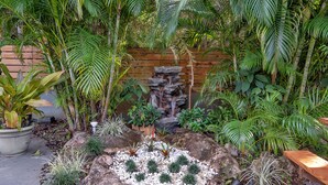A garden with a rock waterfall, various plants, and a wooden bench. - Oasis Hotel (Fort Lauderdale)