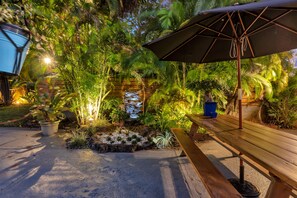 A patio area with a wooden bench, an umbrella, and a small waterfall feature surrounded by lush greenery. - Oasis Hotel (Fort Lauderdale)