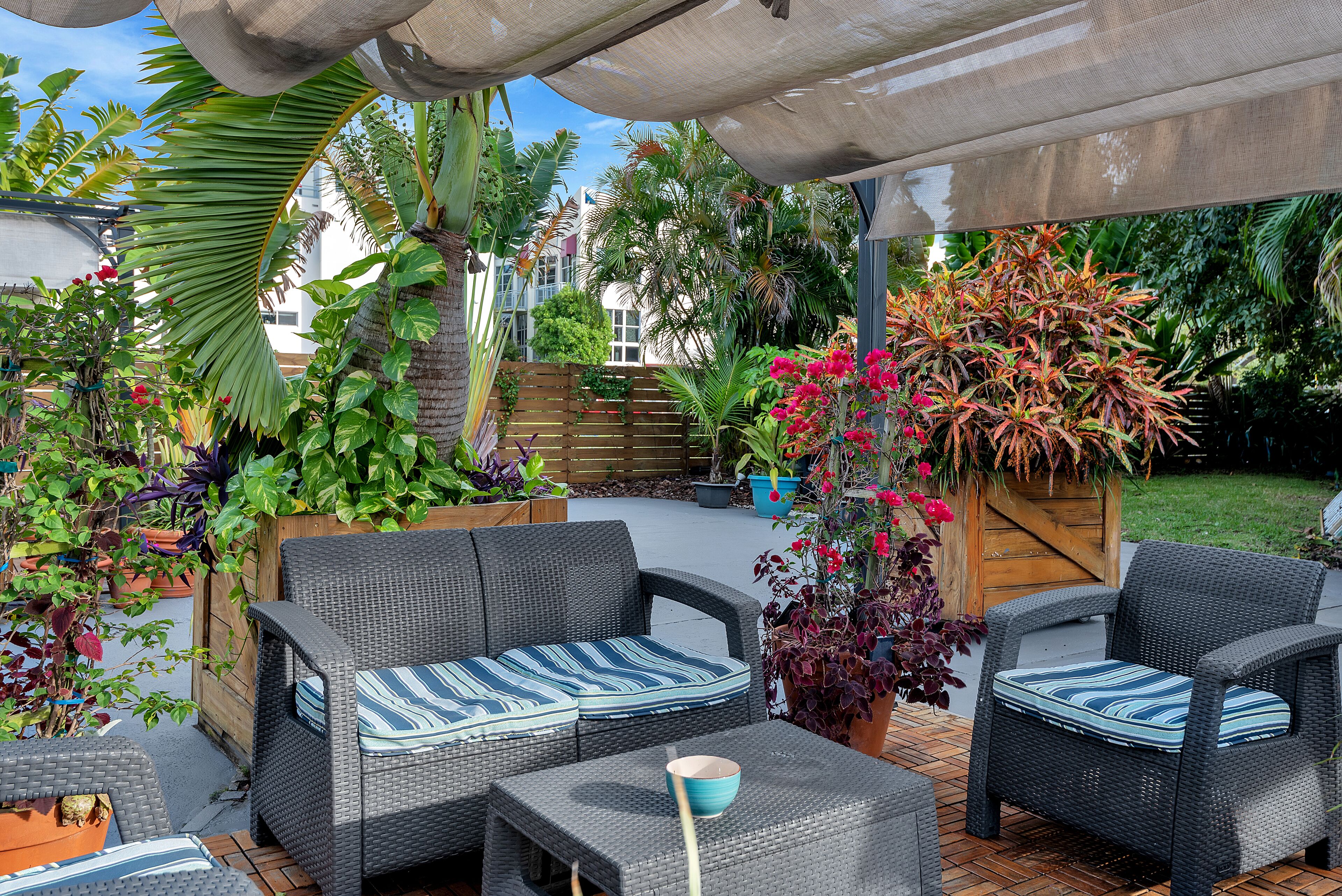 An outdoor patio area with wicker furniture, potted plants, and a wooden fence.