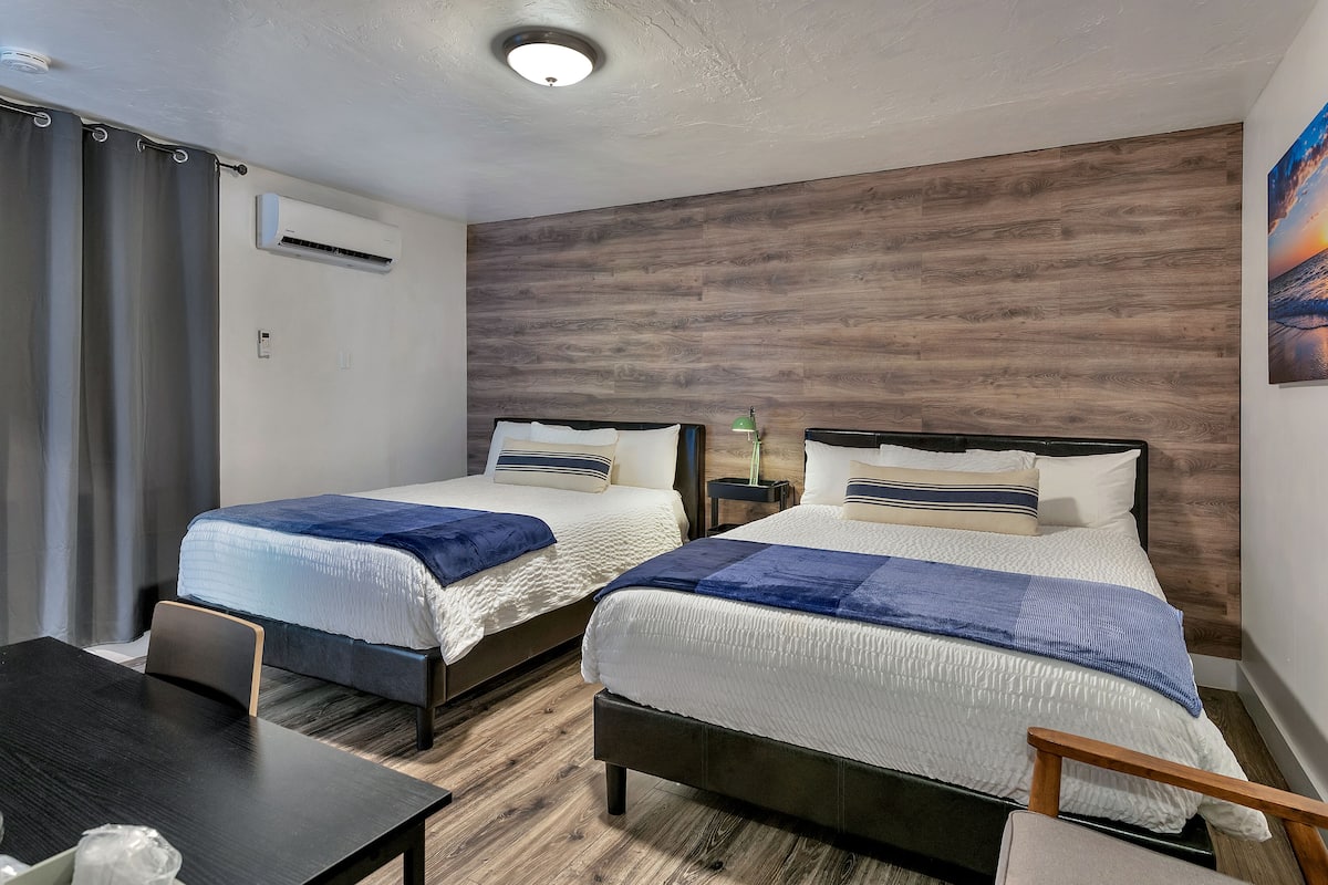 A hotel room with two beds, a desk, and a nightstand.