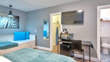 Habitación de hotel con cama, escritorio con silla, microondas, televisión y baño visible a través de una puerta abierta.