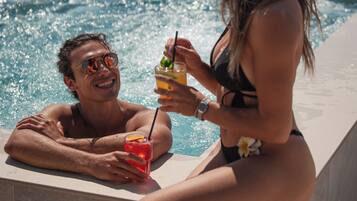 Two people relaxing by a pool with drinks, overlooking a clear blue sky and a distant view.