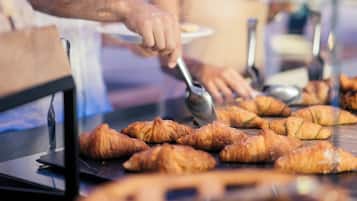 Una persona sirviendo comida detrás de un mostrador de vidrio con cruasanes y un pastel redondo a la vista.
