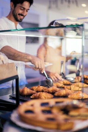 A person serving food behind a glass counter with croissants and a round pastry on display.