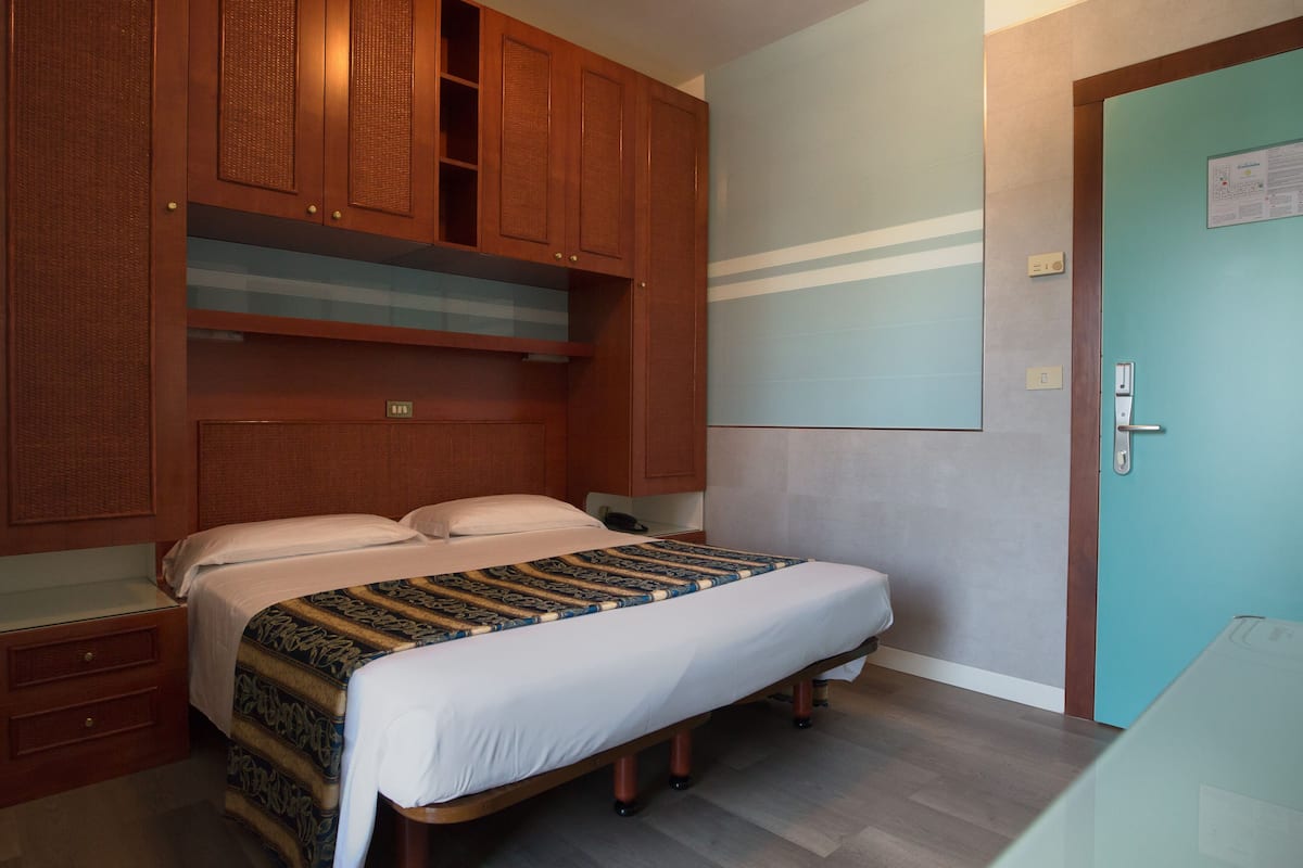 A bedroom with a bed, wooden wardrobe, and a door with a light switch.