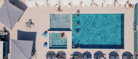 Vista aérea de un área de piscina en la azotea, con varias piscinas, tumbonas y sombrillas.