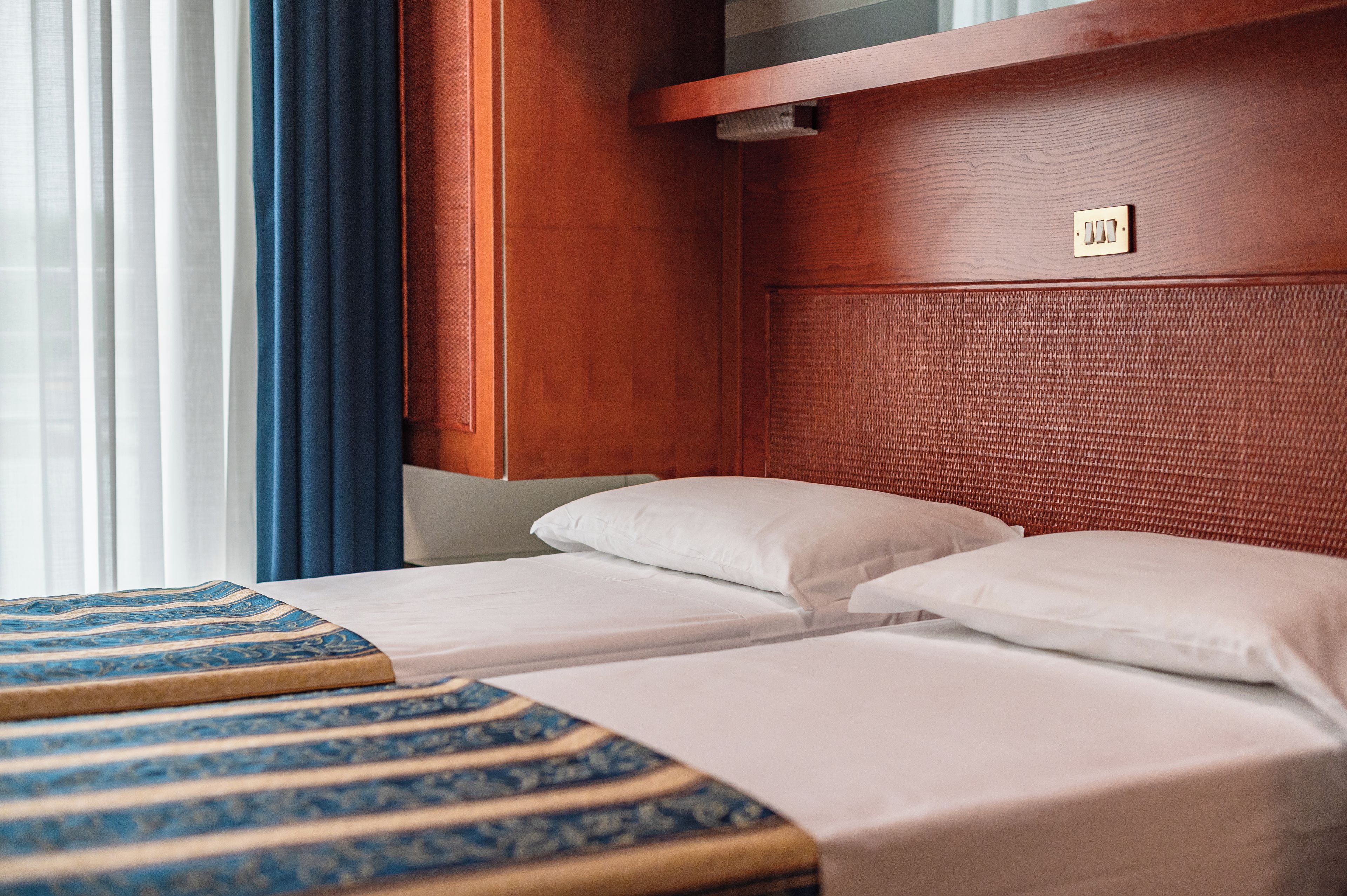A hotel room with two beds, a wooden headboard, and a window with curtains.