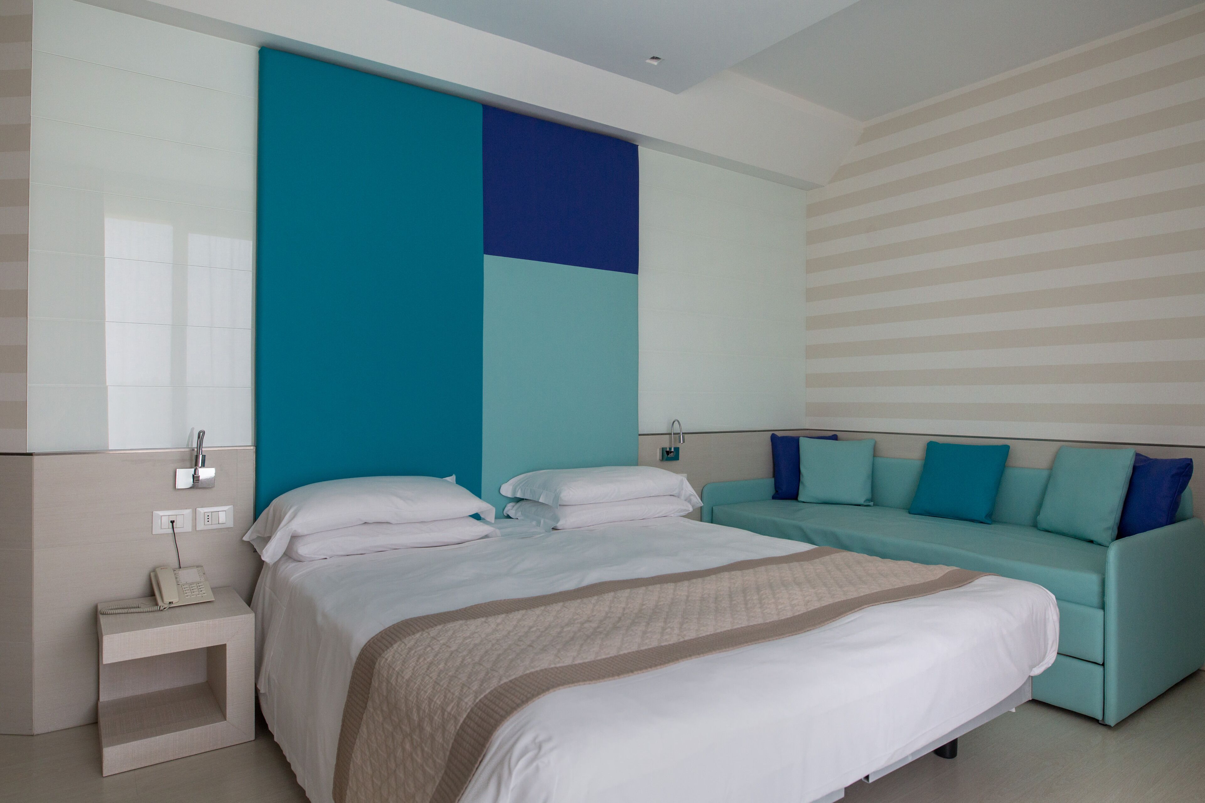A modern hotel room with a large bed, a sofa, and a nightstand with a phone.