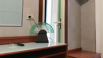 Une pièce avec un bureau en bois, une porte à cadre vert, un téléviseur fixé au mur et une poubelle placée sous le bureau.
