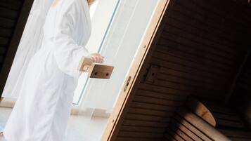 A wooden spa bench with a wooden door and a person in a white robe standing in front of it.