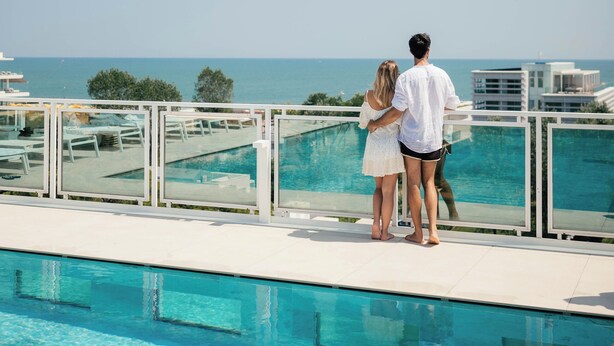 A couple standing by a pool with a view of the sea. - Hotel Colombo (Jesolo)