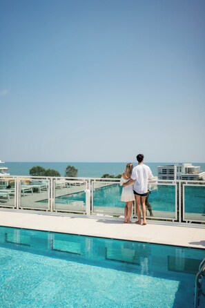 A couple standing by a pool with a view of the sea. - Hotel Colombo (Jesolo)