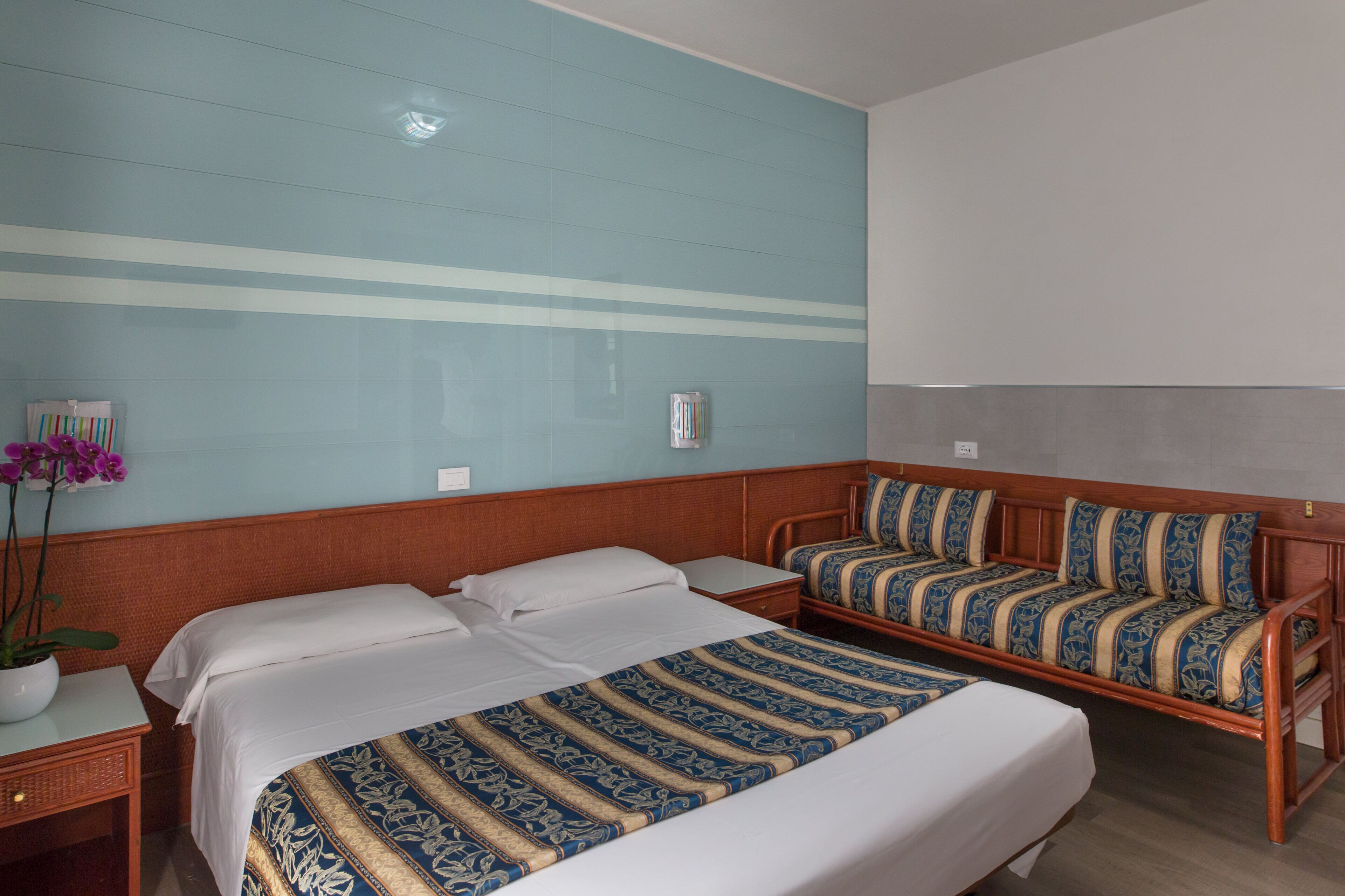 A hotel room with two beds, a sofa, a small table, and a potted plant.