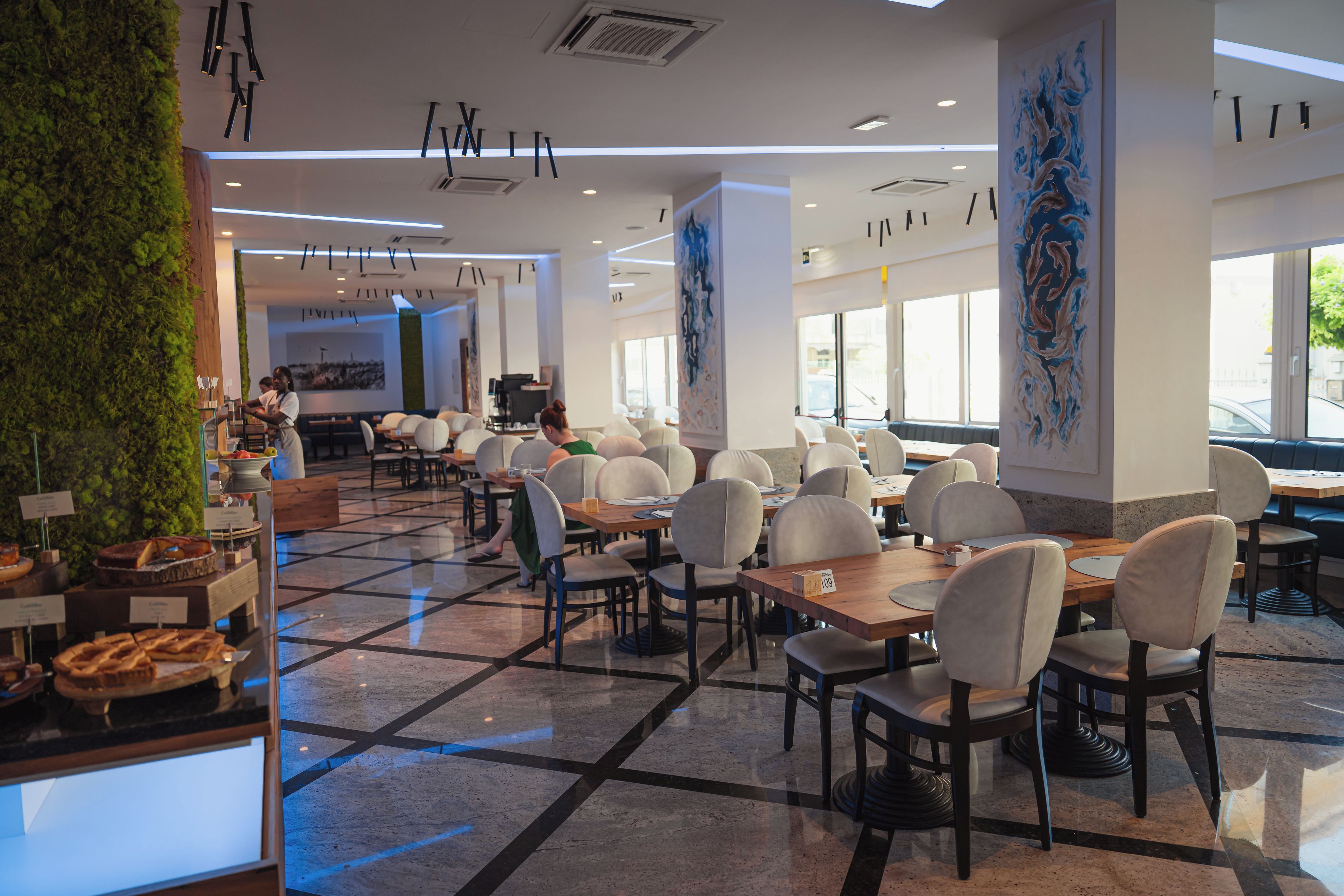 A modern cafe interior with a checkered floor, white chairs, and a green wall.