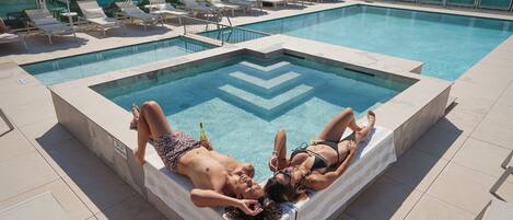 A swimming pool with a geometric tile pattern, surrounded by lounge chairs and umbrellas.