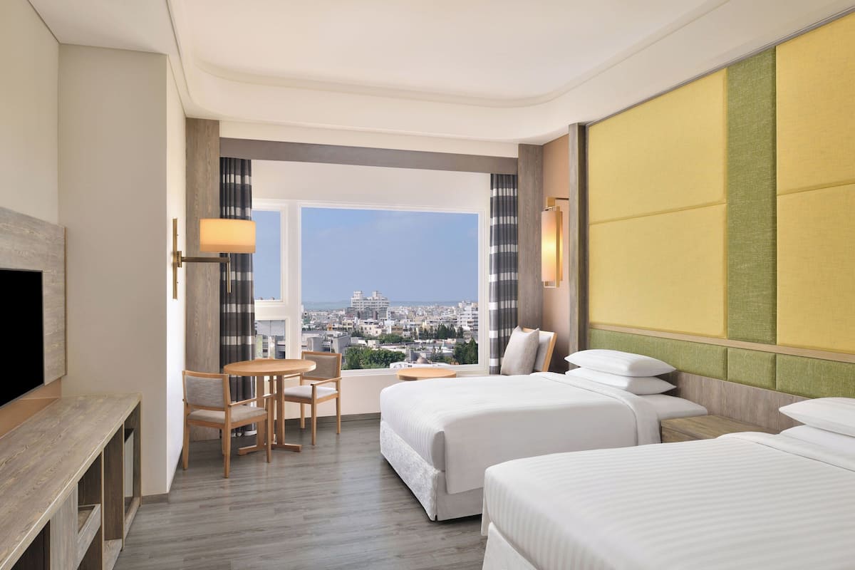 Habitación de hotel con dos camas, un escritorio y una silla. Amplia ventana con vistas a la ciudad.