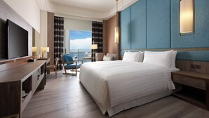 Habitación de hotel con una cama grande, televisión, escritorio con silla y vista al mar.