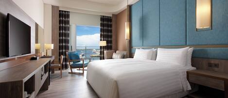 Ein Hotelzimmer mit einem großen Bett, einem Fernseher, einem Schreibtisch mit Stuhl und Blick auf das Meer.