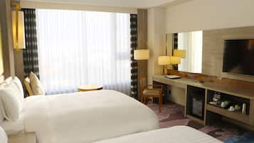A hotel room with two beds, a desk with a chair, a TV, and a minibar.