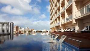 Un hotel con piscina infinita en la azotea, una fila de tumbonas y un paisaje urbano al fondo.