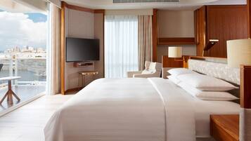 A hotel room with a large bed, a TV, a chair, a desk, and a view of the city.