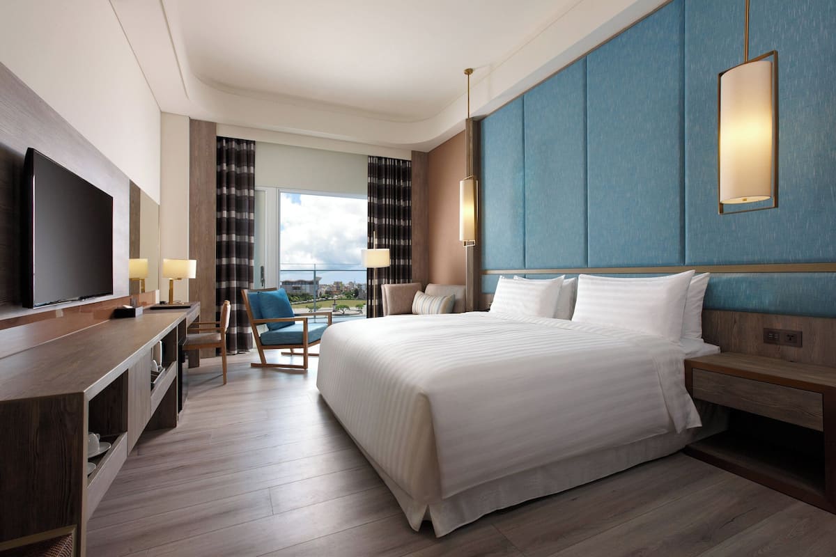 Habitación de hotel con una cama grande, televisión, escritorio con lámpara y vista a la ciudad.