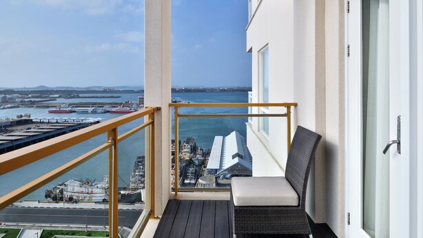 Un balcón con vista a un puerto, una silla y un ventanal.