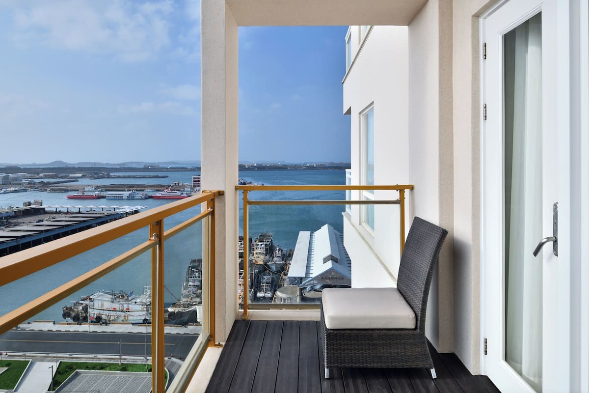 Un balcón con vista a un puerto, una silla y un ventanal.
