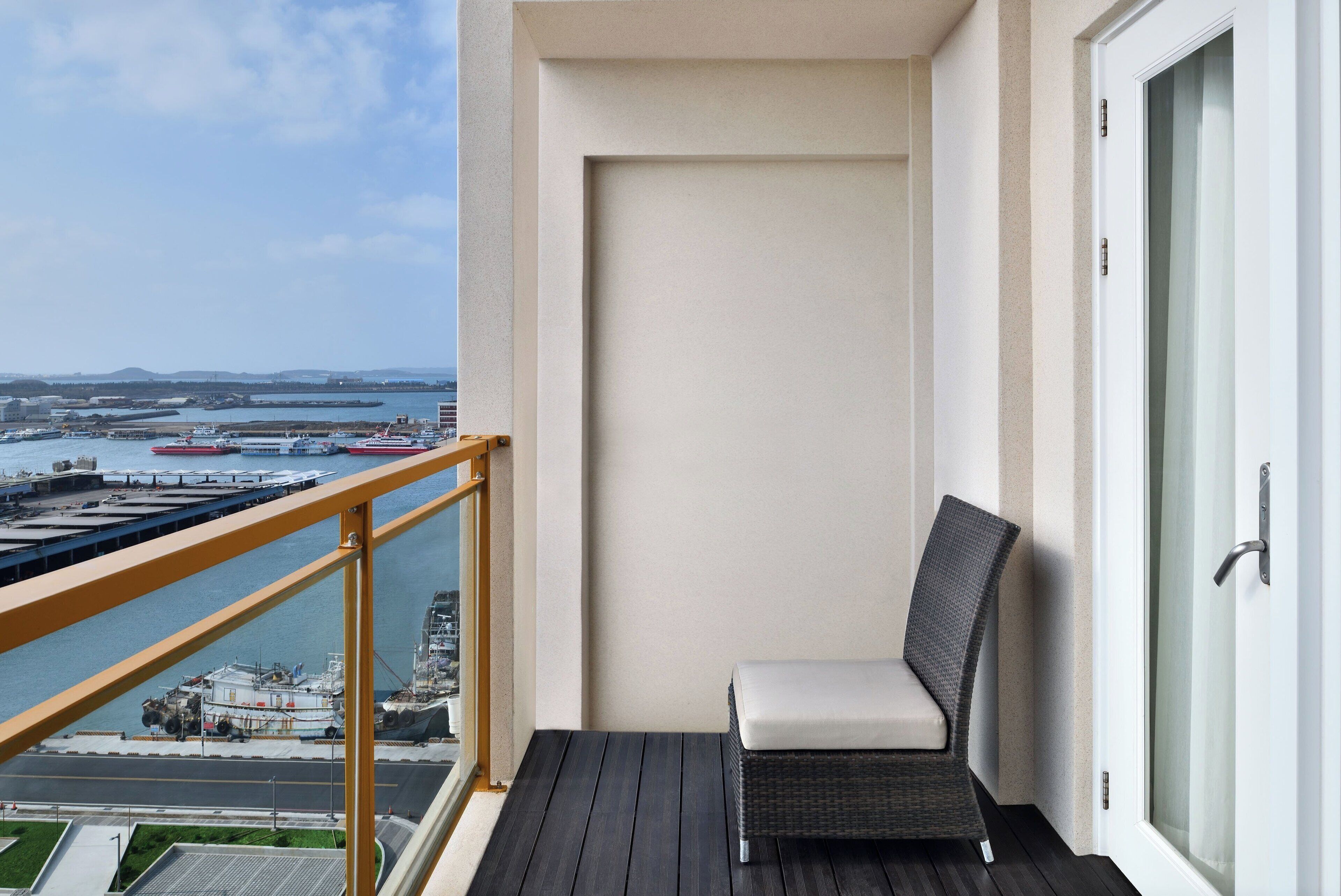 Un balcón con vistas a un puerto y al agua, una silla de mimbre y una puerta con panel de vidrio.