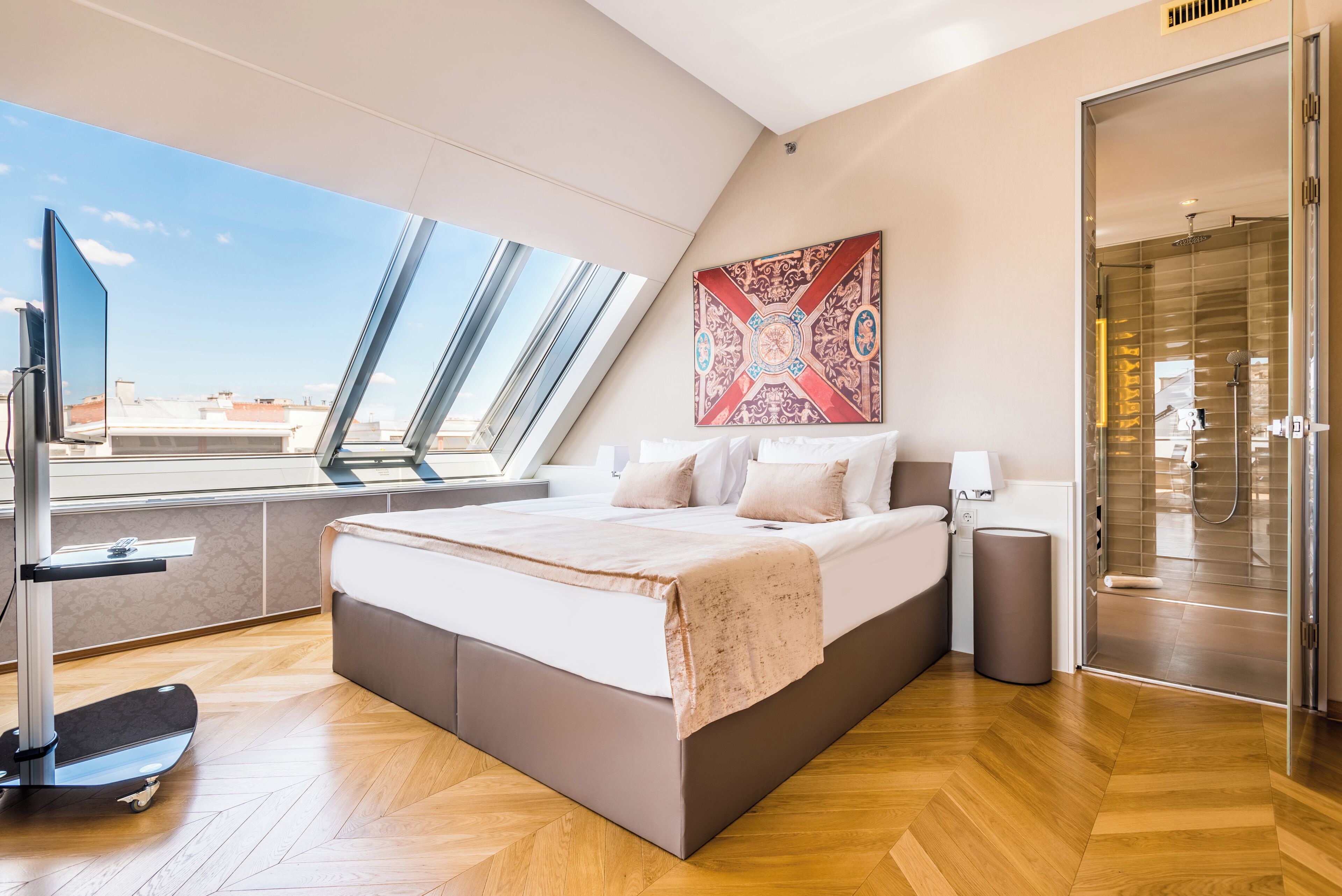 A modern bedroom with a large bed, a skylight, a shower, and a view of the cityscape.