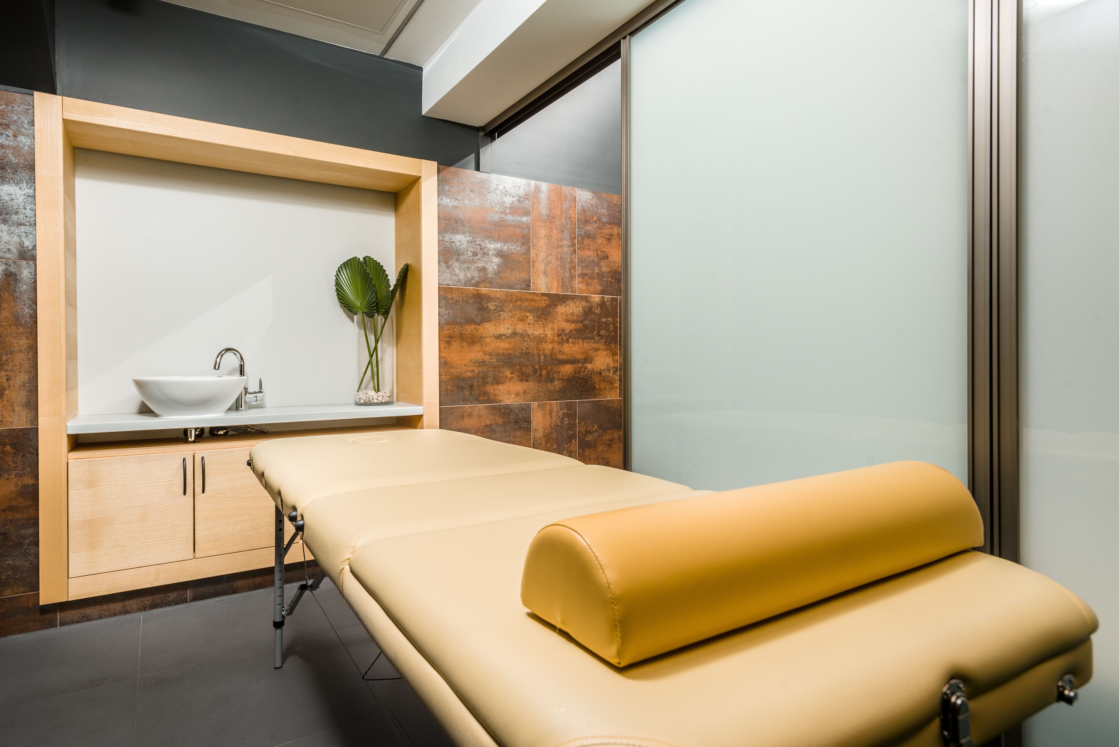 A medical examination room with a wooden cabinet, a white sink, and a yellow examination table.