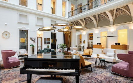 Un amplio vestíbulo con un piano de cola, asientos lujosos y un alto techo con detalles ornamentales.