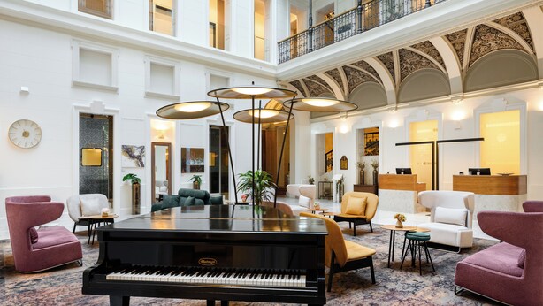 A grand lobby with a grand piano, plush seating, and a high ceiling with ornate detailing. - Hotel Moments Budapest (Budapest)